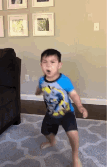 a young boy wearing a batman shirt is dancing in the living room