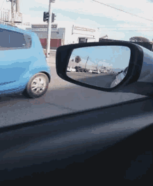 a blue car is driving down a street and is reflected in the rear view mirror of a car