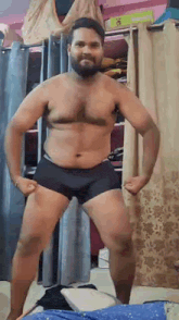 a shirtless man with a beard is standing in a room in underwear .