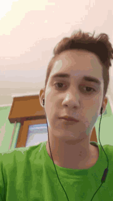 a young man wearing headphones and a green shirt looks at the camera .