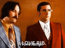 two men in suits and ties are standing next to each other . one of the men is saying `` i love rub '' .