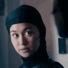 a close up of a woman wearing a black head scarf and a headset