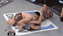two men are wrestling in a boxing ring with 0:38 on the clock