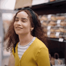 a woman wearing a yellow cardigan and a black headband is smiling in a grocery store .
