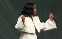 a woman in a white jacket is singing into a microphone on stage .