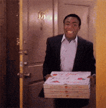 a man in a suit is carrying three pizza boxes and smiling