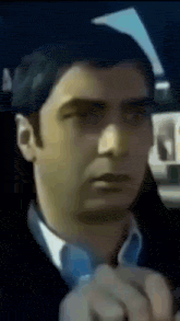 a man in a suit and tie is sitting in a car looking at the camera .