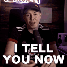 a man in a black adidas shirt is talking into a microphone and says i tell you now