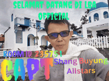 a man wearing sunglasses and a scarf stands in front of a building that says selamat datang di lba on it