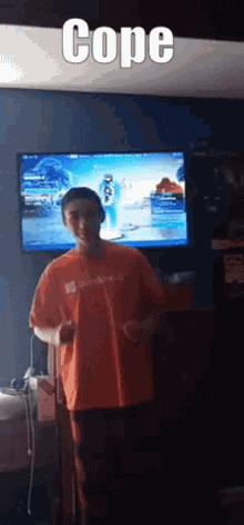 a man in an orange shirt is standing in front of a television with the word cope on it