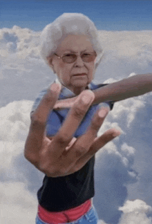 an elderly woman wearing glasses and a black shirt stands in the clouds with her hand outstretched