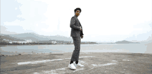 a man in a suit and white sneakers is standing on a concrete platform near the water .
