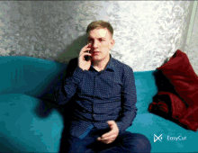 a man is sitting on a blue couch talking on a cell phone with easycut displayed in the corner