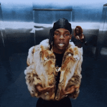 a man in a fur coat stands in an elevator with a woman behind him