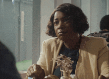 a woman is sitting at a table with a vase of flowers in front of her