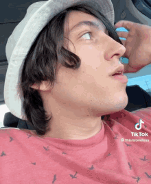 a young man wearing a bucket hat and a red shirt with birds on it has a tiktok on his shirt