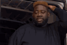 a man with a beard and a black shirt is standing in front of a white van .