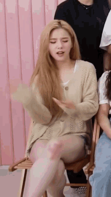 a woman is sitting on a chair with her legs crossed and a cardigan on .