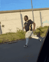 a man in a black and gold shirt is running down a road