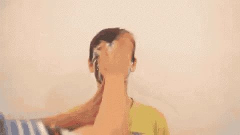 a person is covering a boy 's face with a bucket of shaving cream .