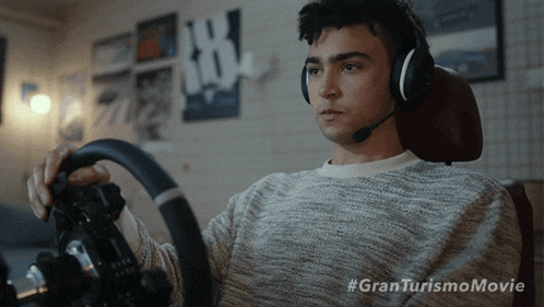 a man wearing headphones and holding a steering wheel with the hashtag #granturismomovie