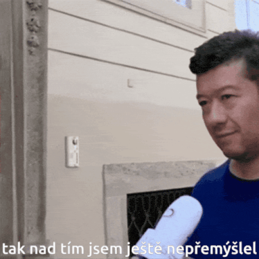 a man in a blue shirt is holding a microphone and says tak nad tim jsem jeste neprmysel