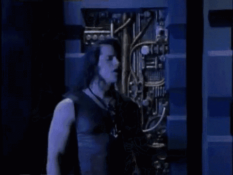 a man in a black tank top with a cross necklace is standing in front of a blue wall .