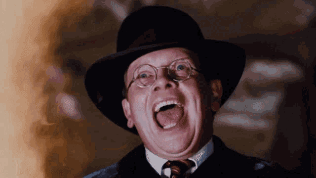 a man wearing glasses and a hat is laughing with his tongue out