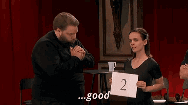 a man stands next to a woman holding a sign with the number 2 on it and says but also quite shrill and bad