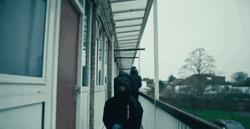 a man in a black hooded jacket is walking down a hallway