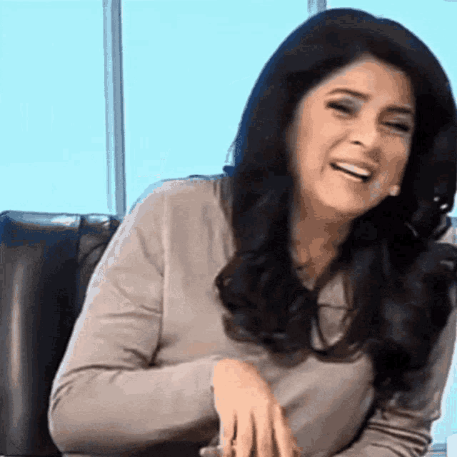 a woman sitting in a chair laughing with her hands folded