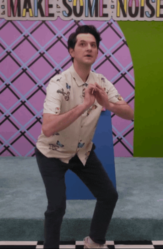 a man is squatting in front of a sign that says " make some noise "