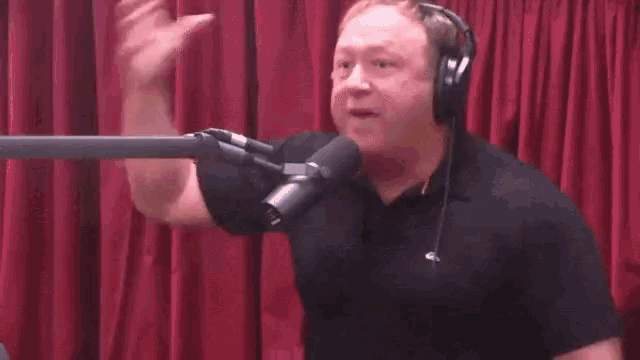 a man wearing headphones stands in front of a microphone in front of a brick wall .