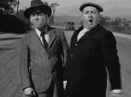 two men in suits and hats are standing next to each other on the side of the road .