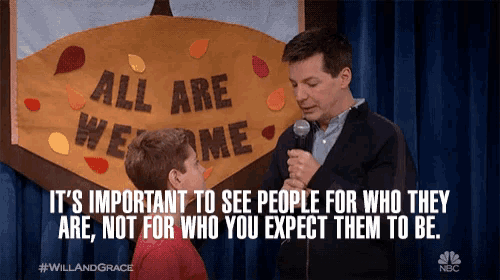 a man speaking into a microphone next to a sign that says all are welcome