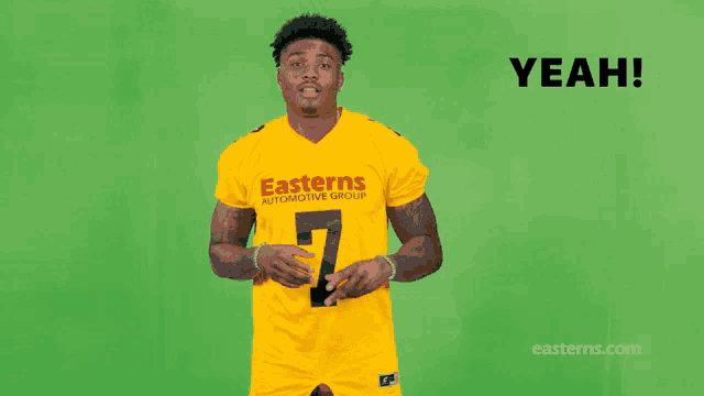 a man wearing a yellow easterns automotive group jersey stands in front of a green background
