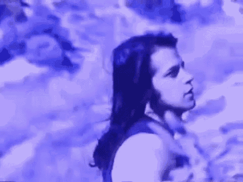 a man with long black hair is standing in front of a purple background .