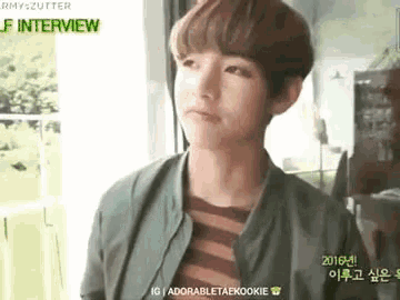 a young man is standing in front of a window wearing a green jacket and a striped shirt .