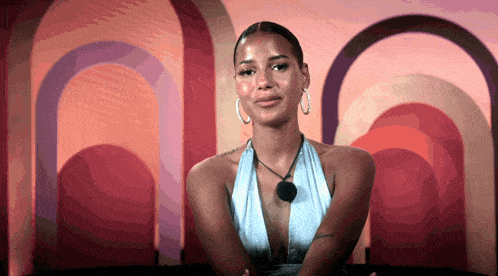 a woman wearing a blue top and hoop earrings is sitting in front of a colorful wall