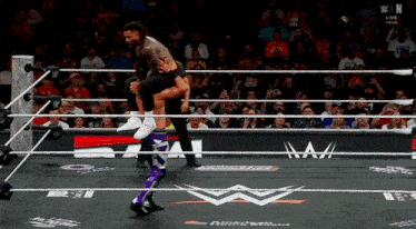 a wrestler is being lifted in the air by another wrestler in front of a crowd