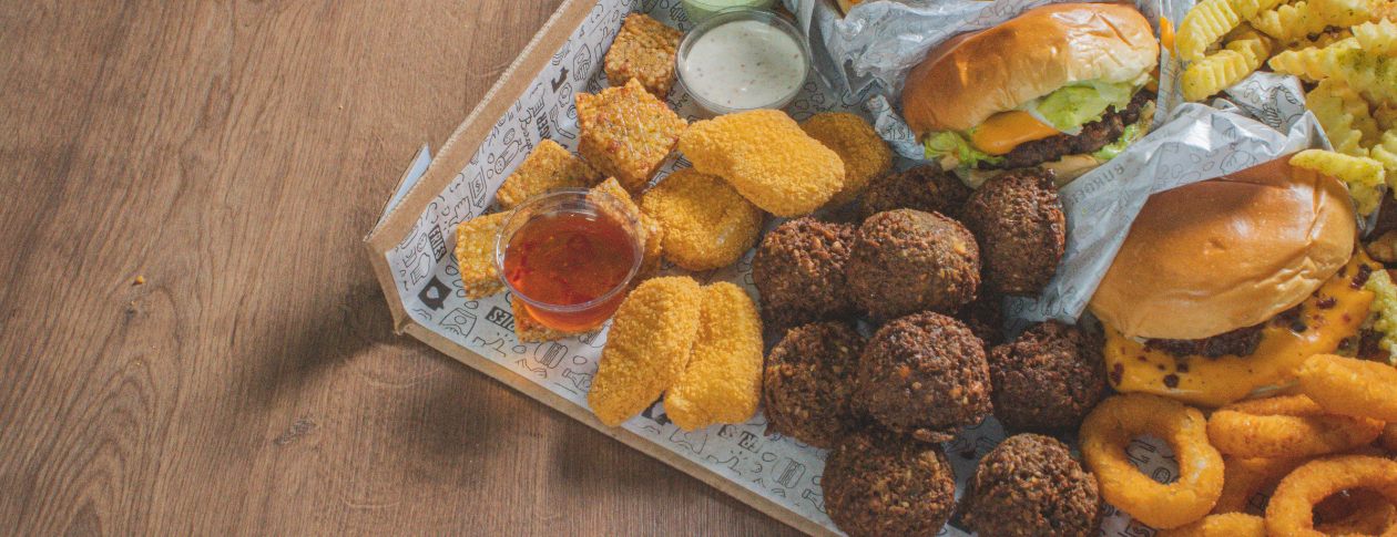 Close up of a tray of fast food, consisting of burgers, chicken nuggets, onion rings, french fries, and falafel