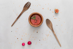 Una ciotola di salsa di pomodoro, forchetta e cucchiaio di legno, un ravanello e un fico