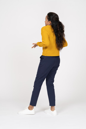 Vista posterior de una niña en ropa casual de pie con los brazos extendidos