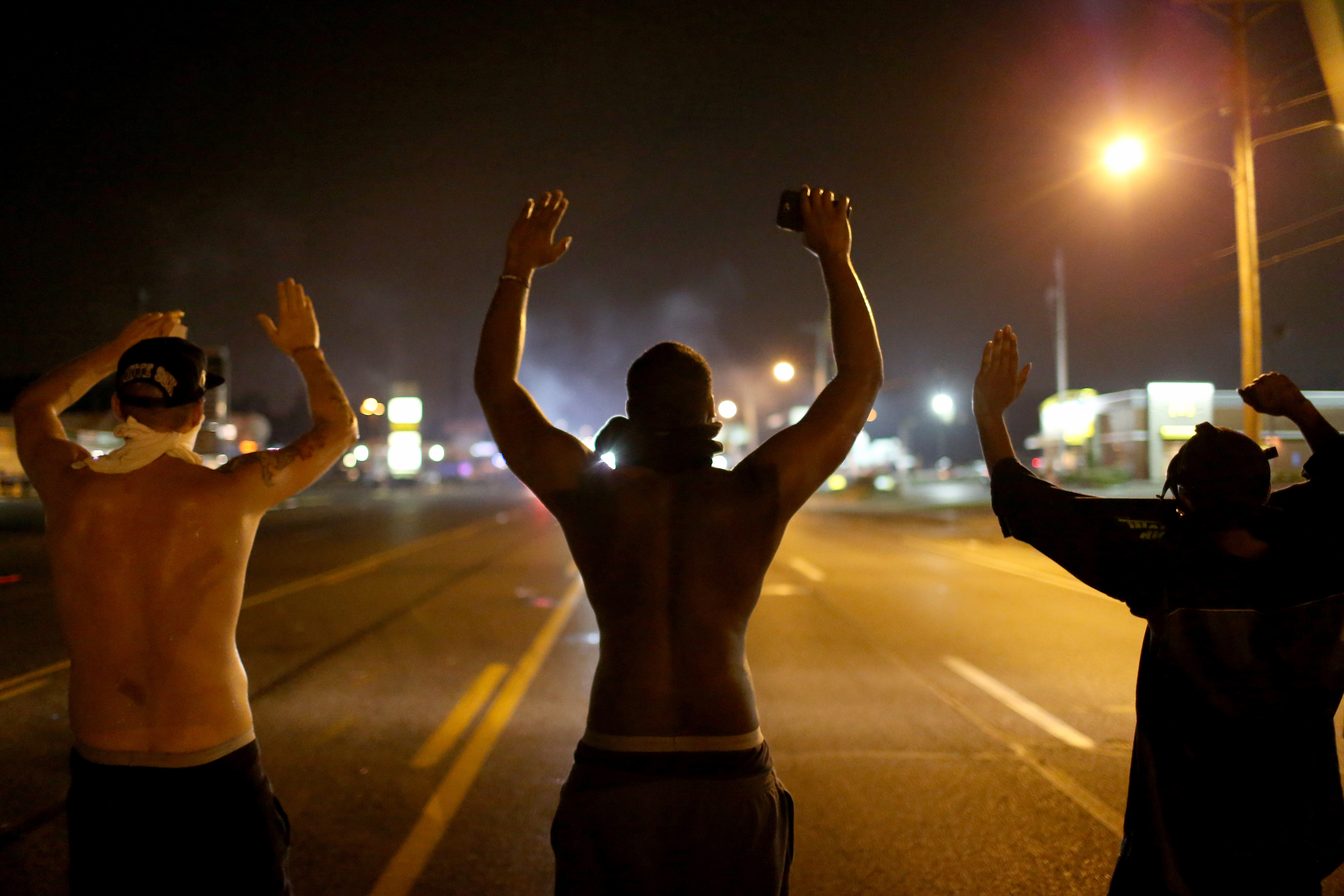 FERGUSON, MO - AUGUST 17: Demonstrators raise their arms and chant, "Hands up, Don't Shoot", as police clear them from the street as they protest the shooting death of Michael Brown on August 17, 2014 in Ferguson, Missouri. Police sprayed pepper spray, shot smoke, gas and flash grenades as violent outbreaks have taken place in Ferguson since the shooting death of Michael Brown by a Ferguson police officer on August 9th. (Photo by Joe Raedle/Getty Images)
