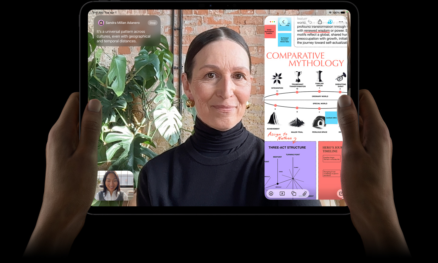 Asztrofekete iPad Pro elölnézetből, lekerekített sarkokkal, fekete kijelzőkerettel. Bal és jobb kézzel fekvő tájolásban tartják, a kijelzőn élőben fordított FaceTime-beszélgetés, valamint egy oktatási célú alkalmazás jelenik meg, amely egy összehasonlító mitológiáról szóló prezentációt tartalmaz szöveggel, ábrákkal és kézzel írt jegyzetekkel