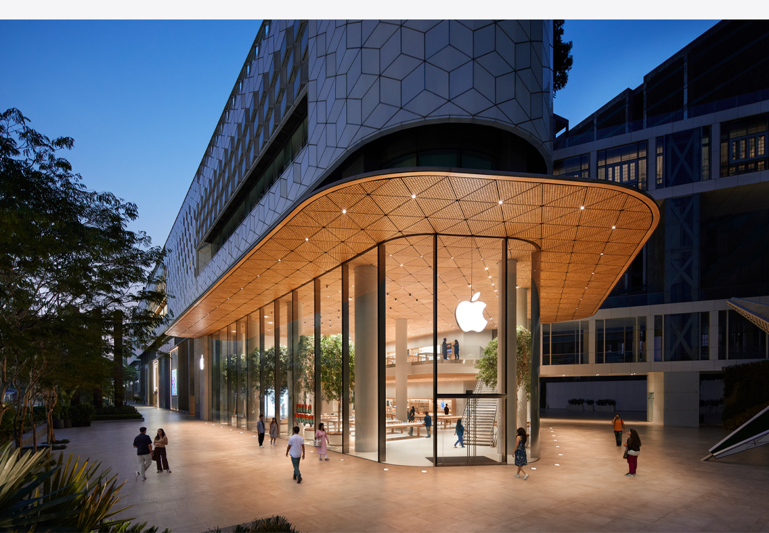 Apple Store le soir, fenêtres vitrées, éclairage à l’intérieur, logo Apple centré sur la partie supérieure de la porte avant.