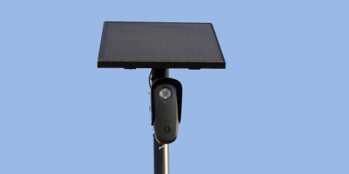 A Flock Safety camera beneath a solar panel on a pole