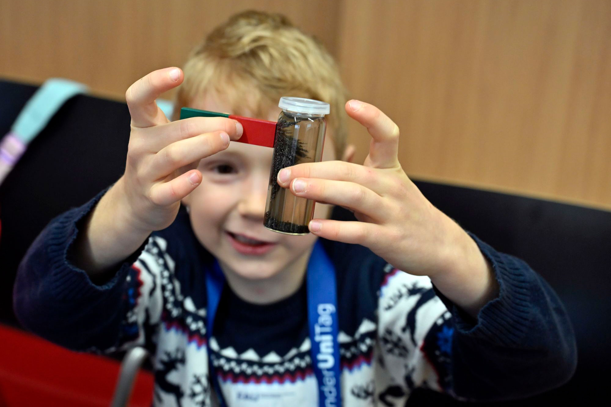 Kind hält Magnet an Glas das Flüssigkeit und eine magnetische Substanz enthält. Kinderuni der FAU
