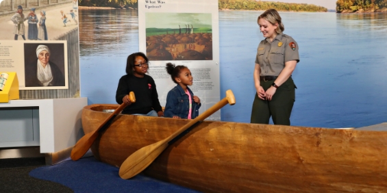 mother and daughter in the canoe featured in the museum with a NPS ranger talking to them.