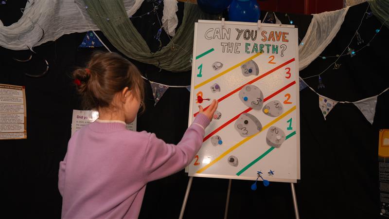 small female child throwing a dart at a board with can you save the earth written on it